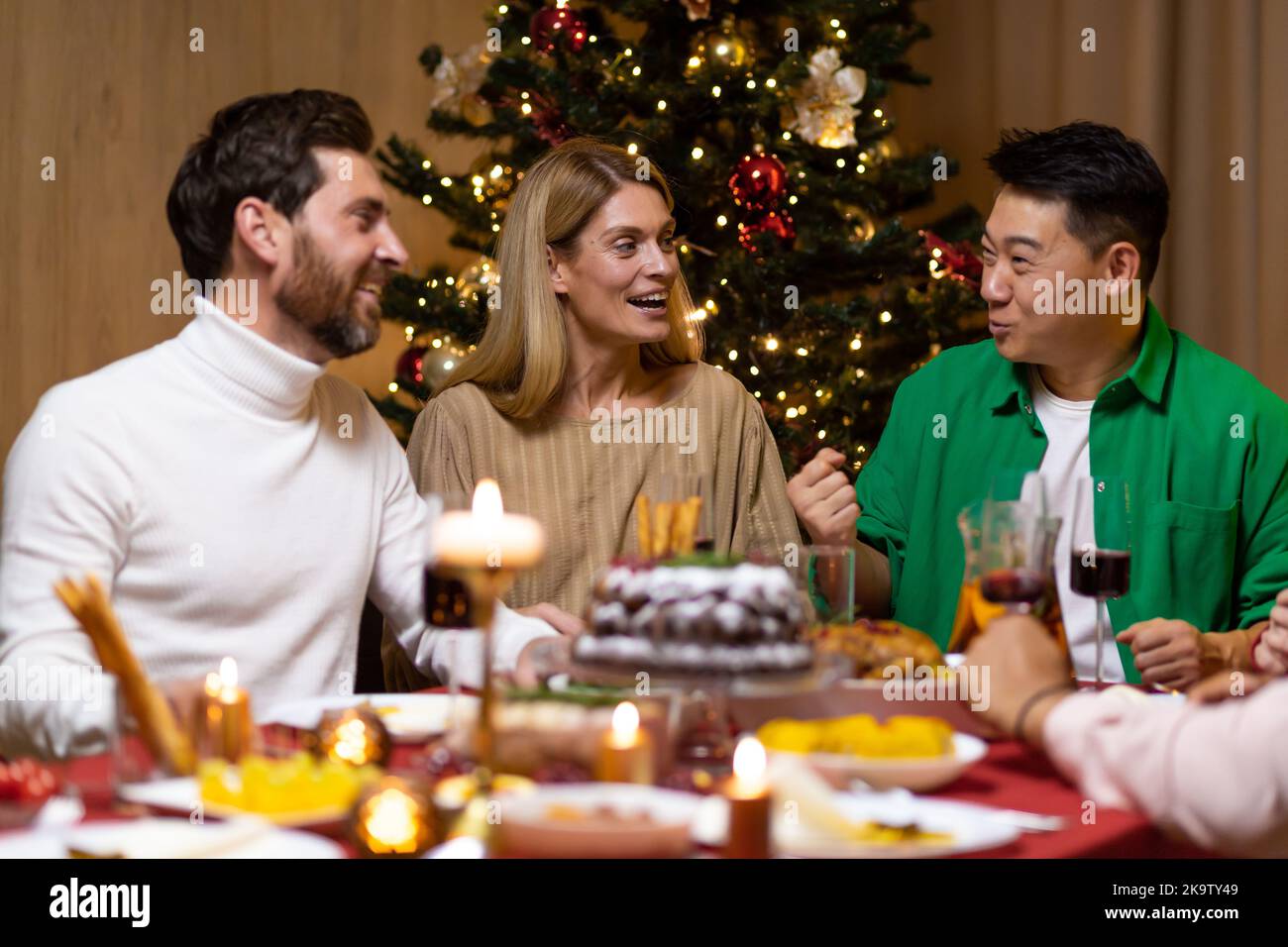 Les amis fêtent la veille de Noël ou le jour de l'an ensemble assis à la table. Dégustez un dîner de noël composé de plusieurs groupes ethniques. Des gens joyeux et joyeux. Banque D'Images
