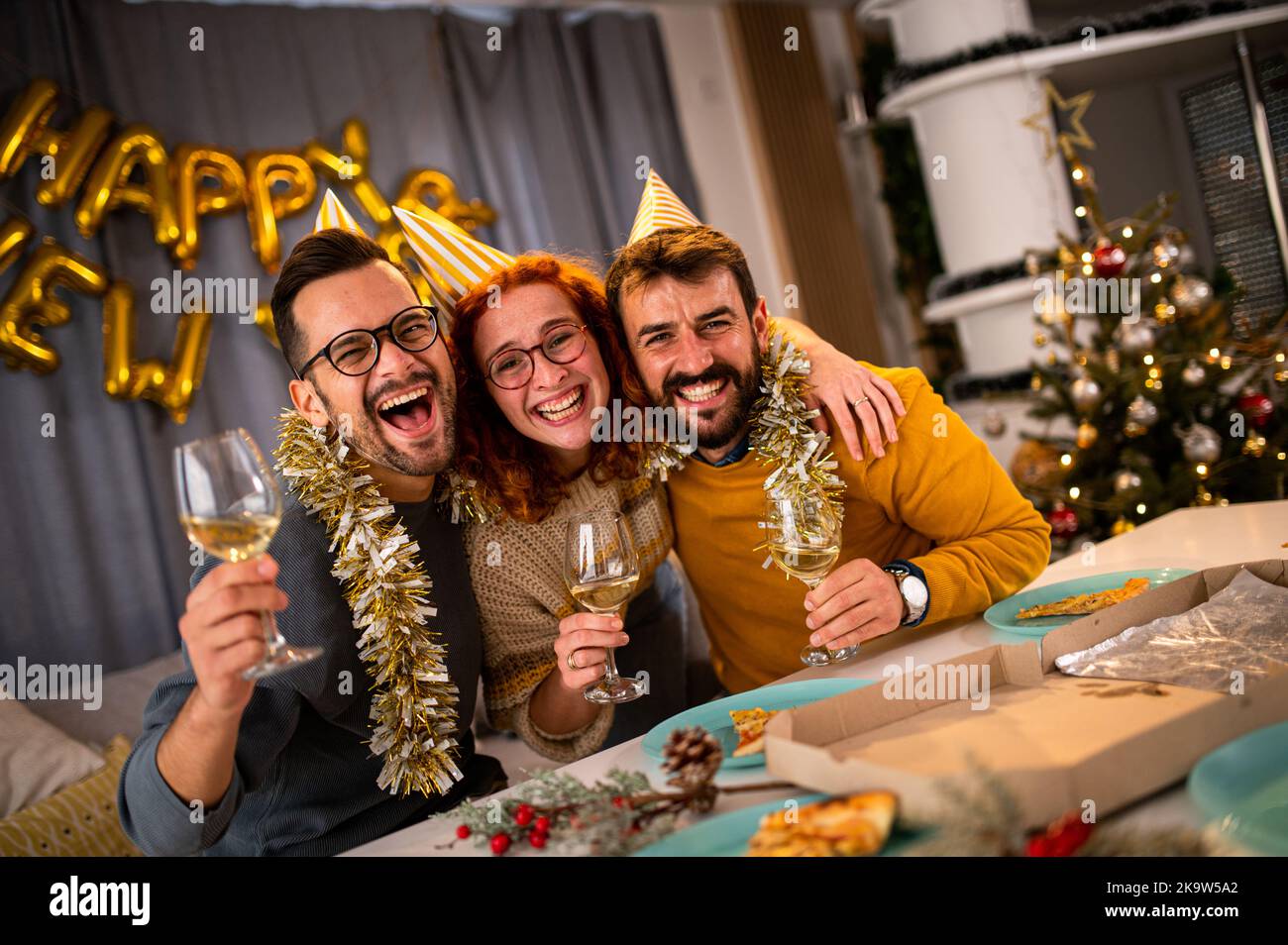 Les jeunes qui regardent la caméra sourient et rient à la fête du nouvel an en buvant du vin et du champagne. Banque D'Images