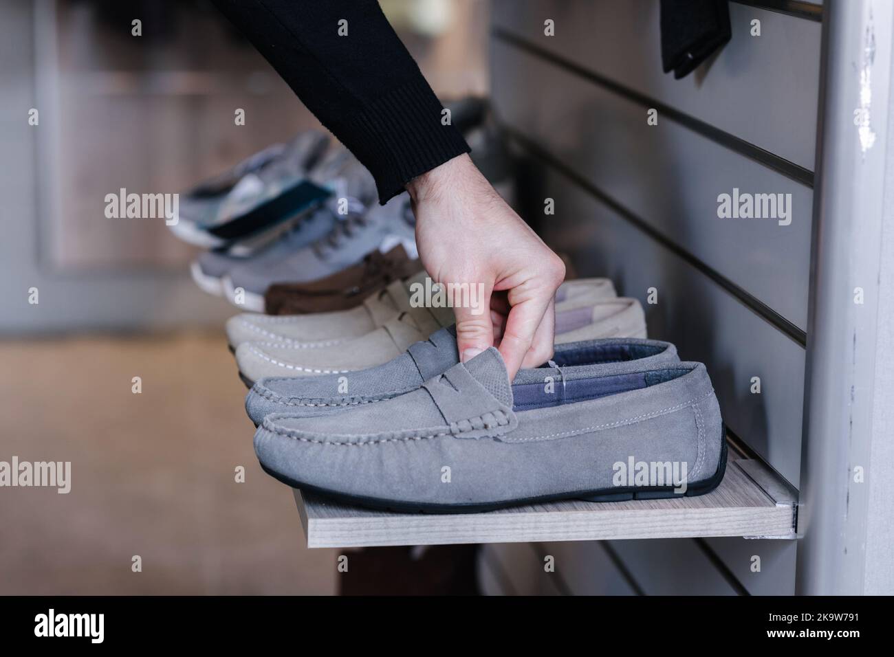 Main de l'homme prenant des mocassins gris de l'étagère dans le magasin de vêtements. Vue latérale Banque D'Images