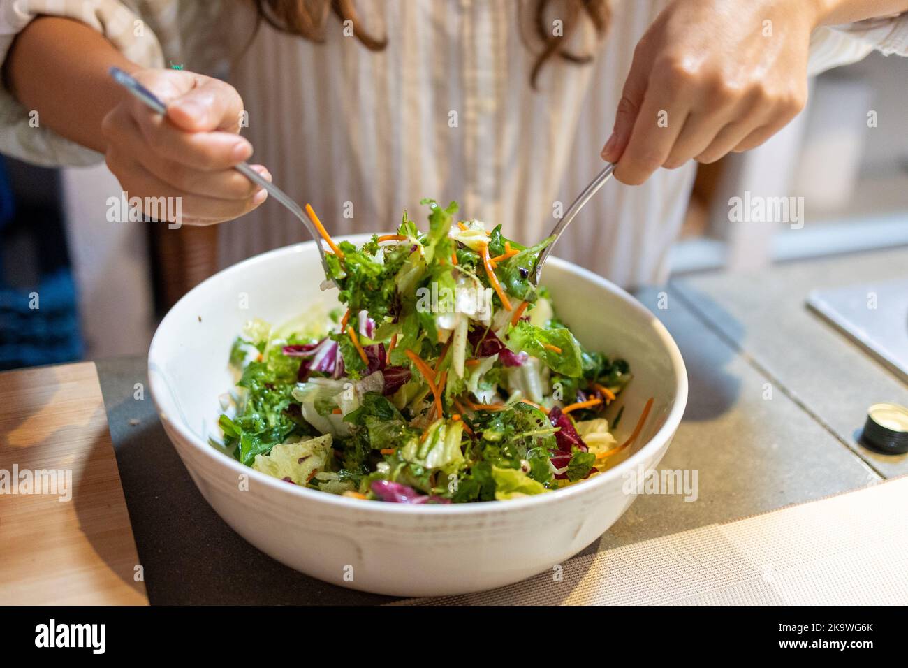 Les mains des femmes mélangent la salade verte dans le bol avec des fourchettes Banque D'Images