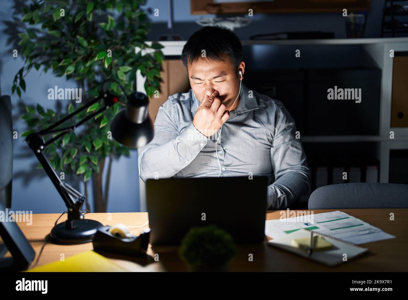 Un jeune homme chinois qui travaille avec un ordinateur portable la nuit  sentait quelque chose d'original et de dégoûtant, une odeur intolérable,  qui retient l'haleine avec les doigts sur n Photo Stock -