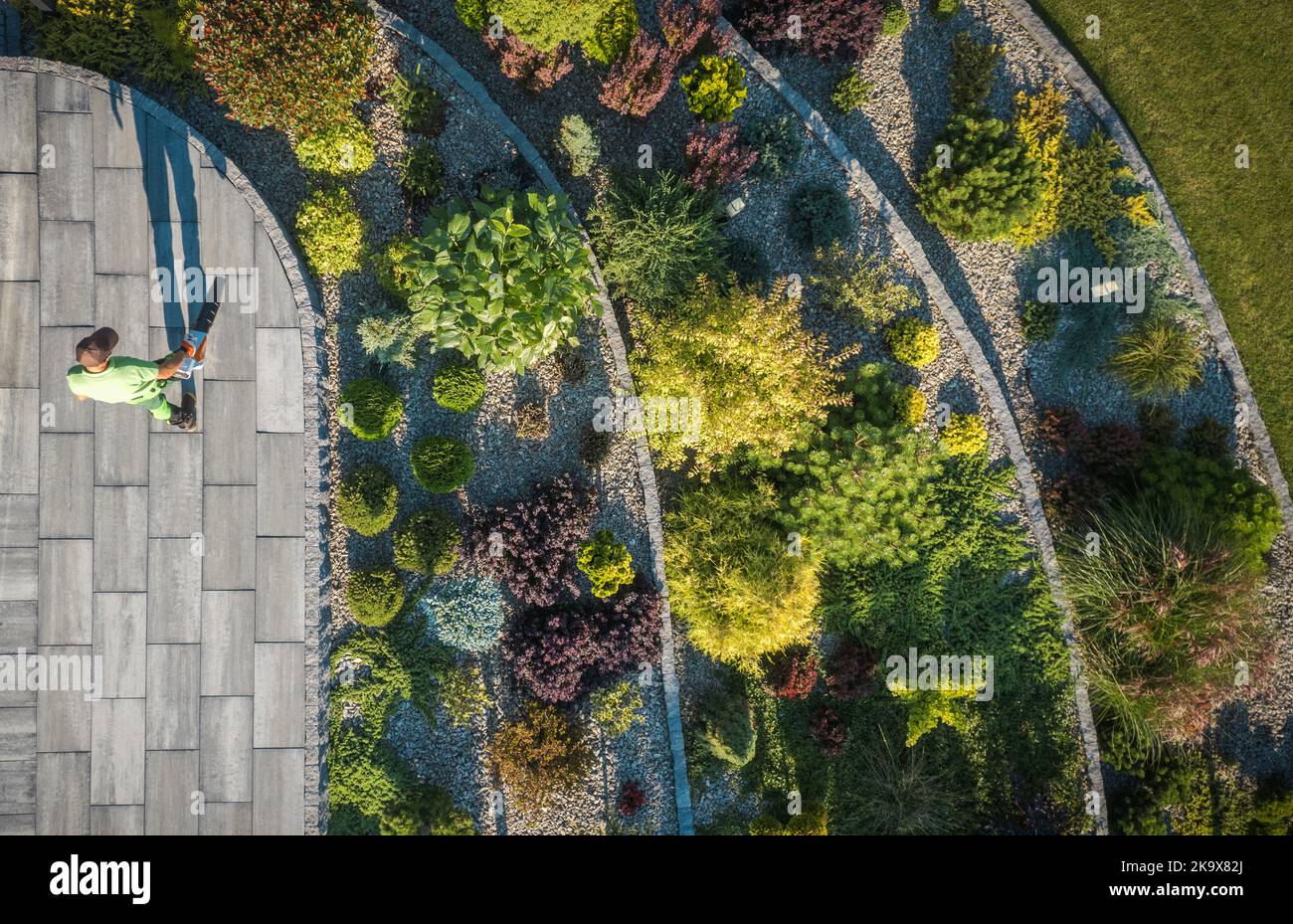 Vue aérienne du jardin résidentiel de Rockery et de l'homme soufflant des feuilles d'un chemin. Industrie de l'aménagement paysager et du jardinage. Banque D'Images