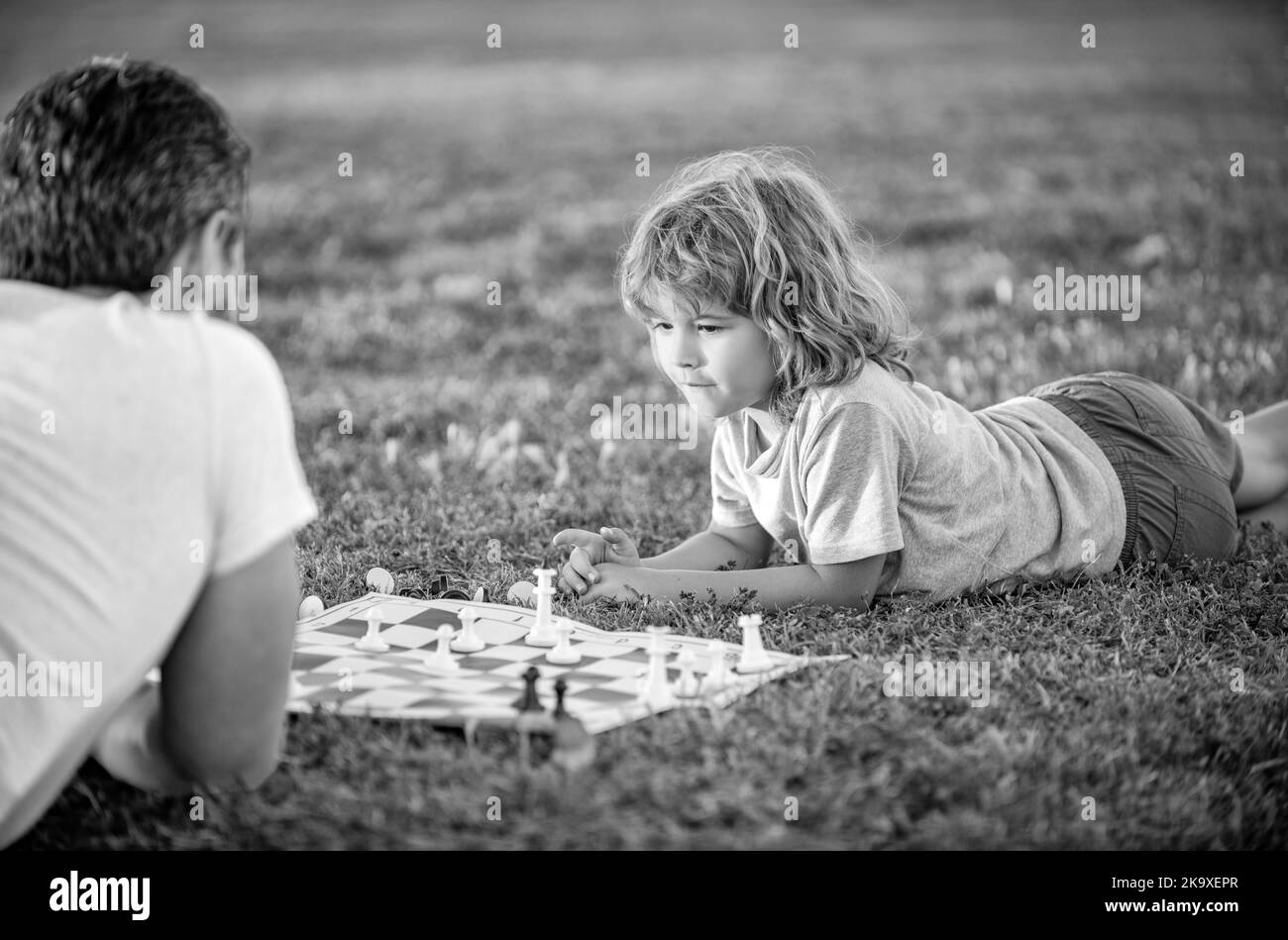 famille heureuse de parents et d'enfants jouant aux échecs sur l'herbe verte dans le parc extérieur, relations familiales. Banque D'Images