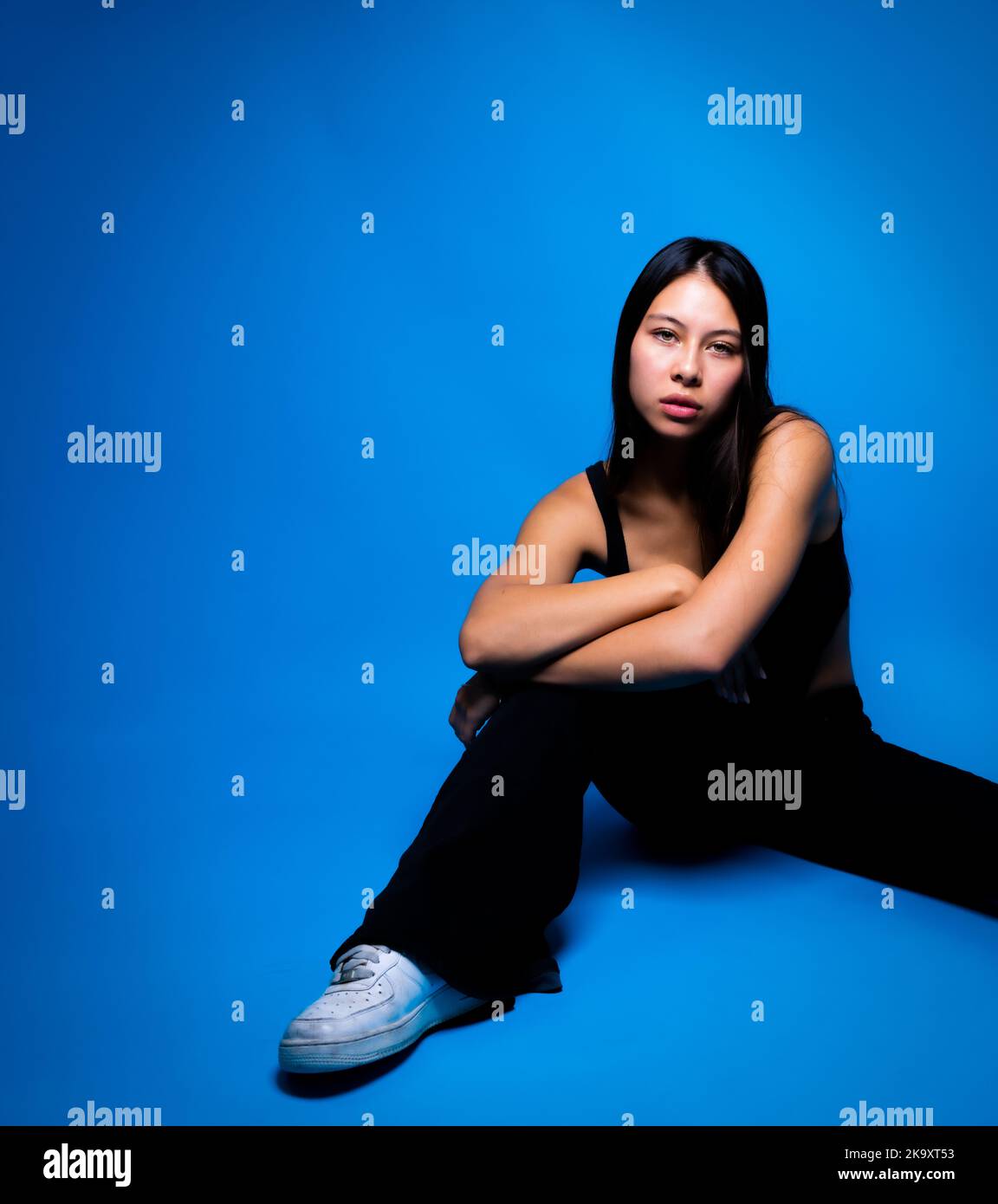 Sérieuse recherche multiraciale jeune femme assise avec espace pour la copie sur fond bleu Banque D'Images