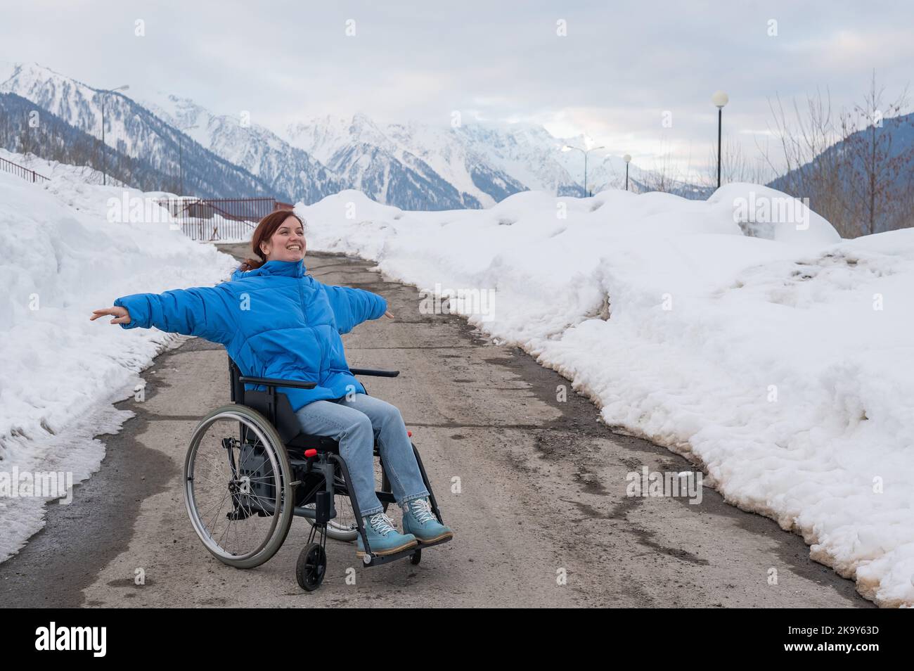 Une femme en fauteuil roulant a étendu ses bras sur le côté comme des ailes dans les montagnes en hiver. Banque D'Images