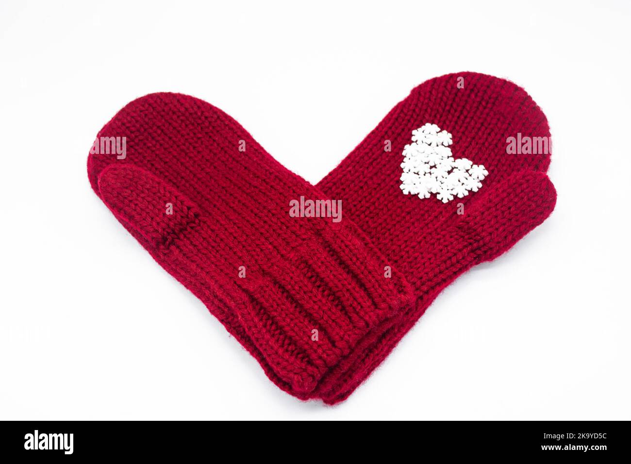 Deux moufles rouges tricotées sont l'une l'autre avec des flocons de neige blancs en forme de coeur.Arrière-plan blanc, isolé.Concept de Noël, hiver, lo Banque D'Images