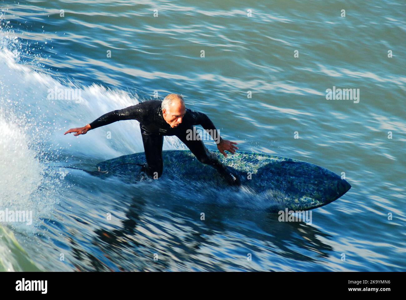 Un homme senior prend une vague sur sa planche de surf, en restant en bonne santé et actif tout en surfant dans l'océan au large de la côte californienne Banque D'Images