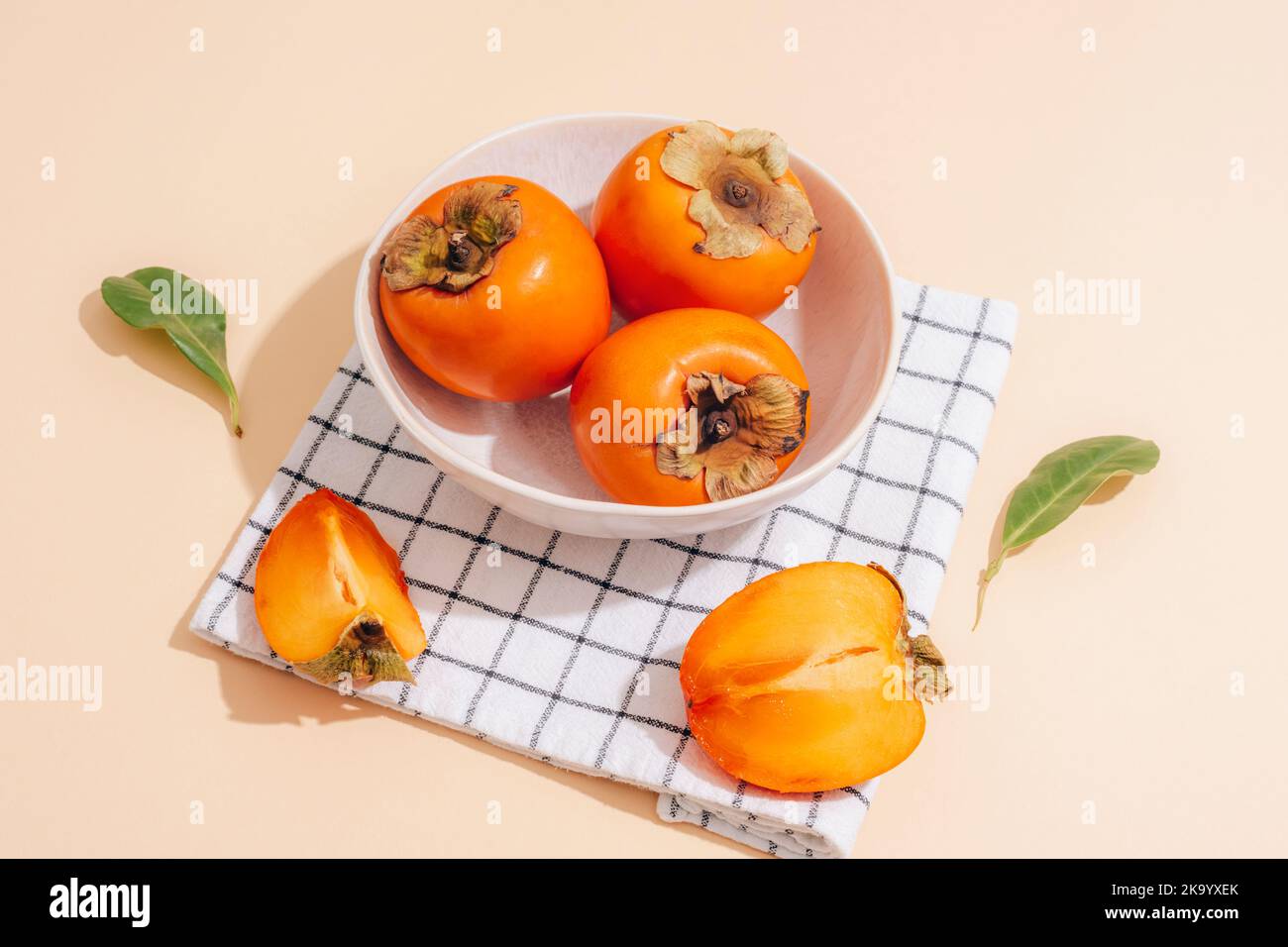 Des permmons mûrs frais dans un bol blanc et une serviette à carreaux sur fond beige. Concept alimentaire végétalien sain. Vue de dessus. Banque D'Images