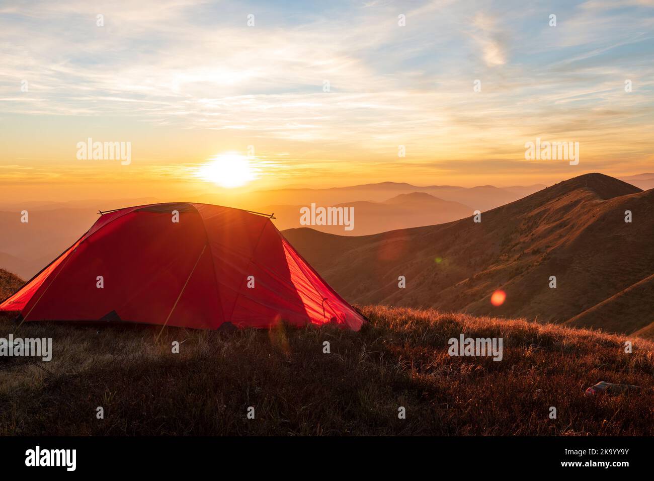 Tente rouge de randonnée sur le sommet de la montagne au coucher du soleil. Des vacances en plein air incroyables Banque D'Images