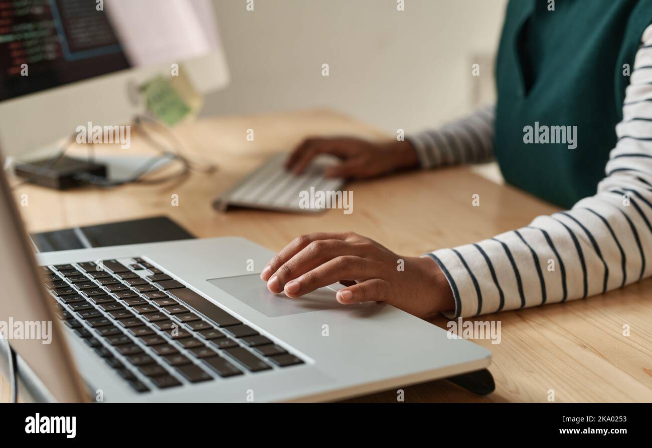 Main de la jeune femme noire sur le pavé tactile d'ordinateur portable pendant le réseau ou la création de nouveau site Web tout en étant assis au bureau sur le lieu de travail Banque D'Images