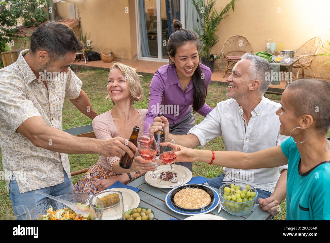 Groupe multiculturel d'amis gaies en dégustant avec un beau sourire autour de la table à la maison patio dîner. Banque D'Images