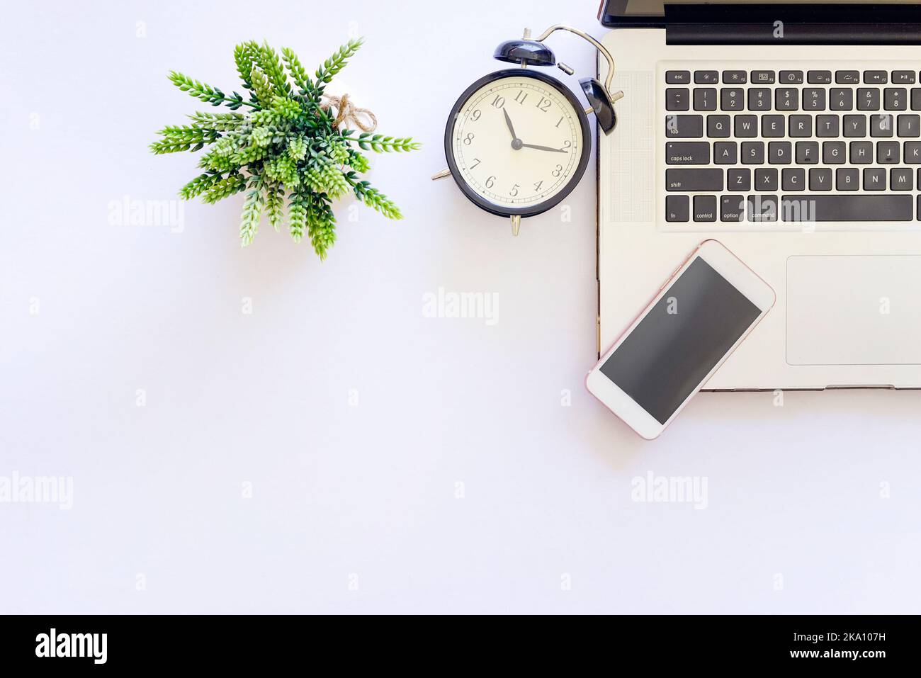 Plan de travail à plat vue du dessus d'une table blanche avec un ordinateur portable, un stylo, un smartphone et une plante verte Banque D'Images