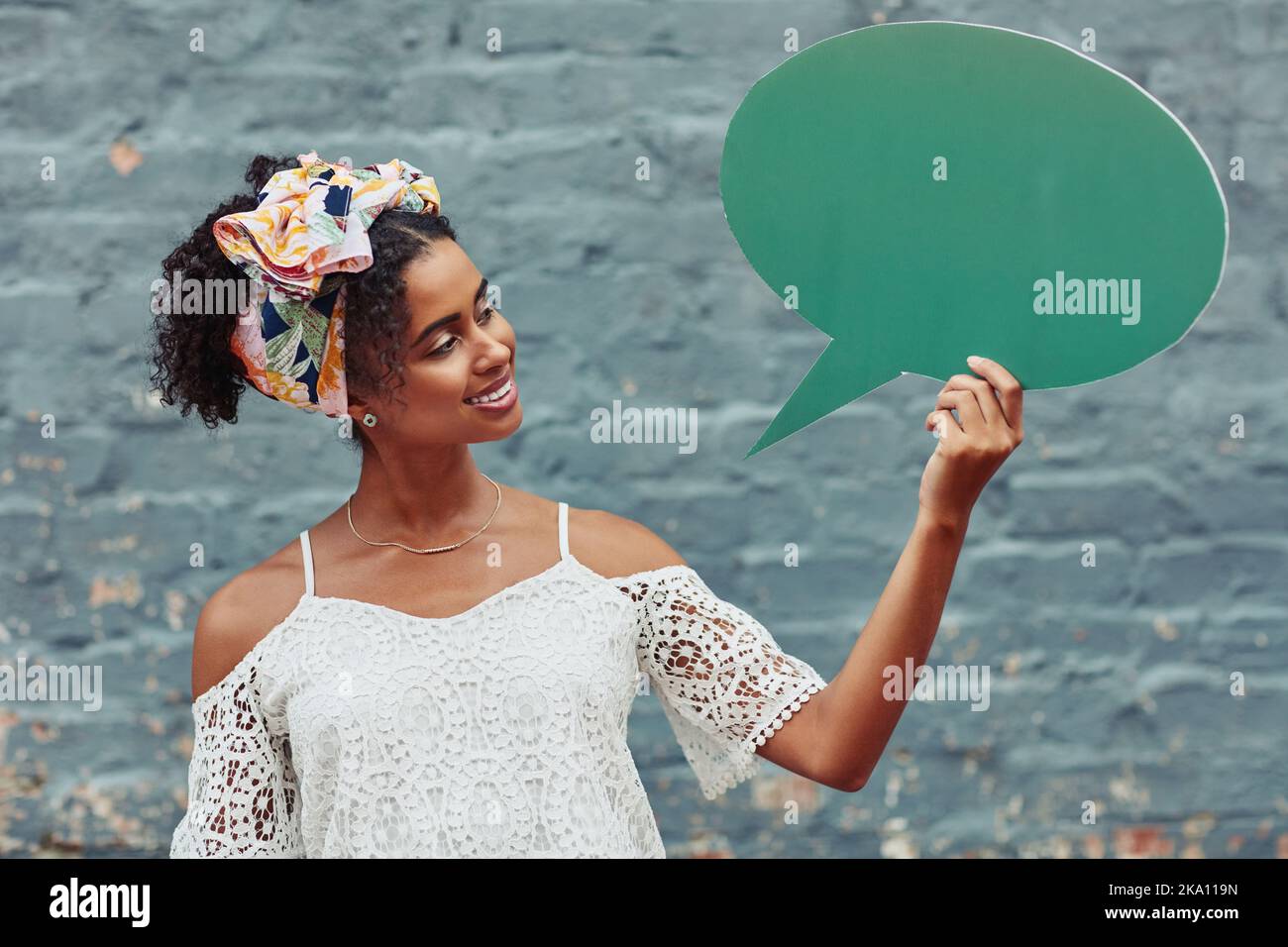 Aimez les mots que vous parlez en étant toujours aimable. Une jeune femme attrayante tenant une bulle de discours contre un mur de briques à l'extérieur. Banque D'Images