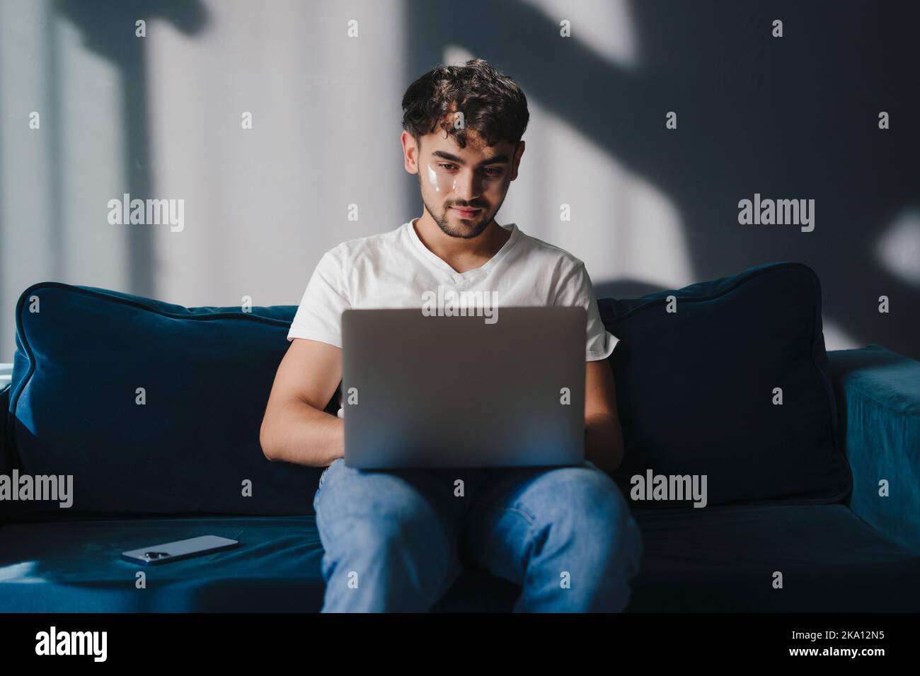 Jeune homme attrayant se reposant sur un canapé à la maison, tenant, utilisant et travaillant sur un ordinateur portable passer son temps libre dans le salon Banque D'Images