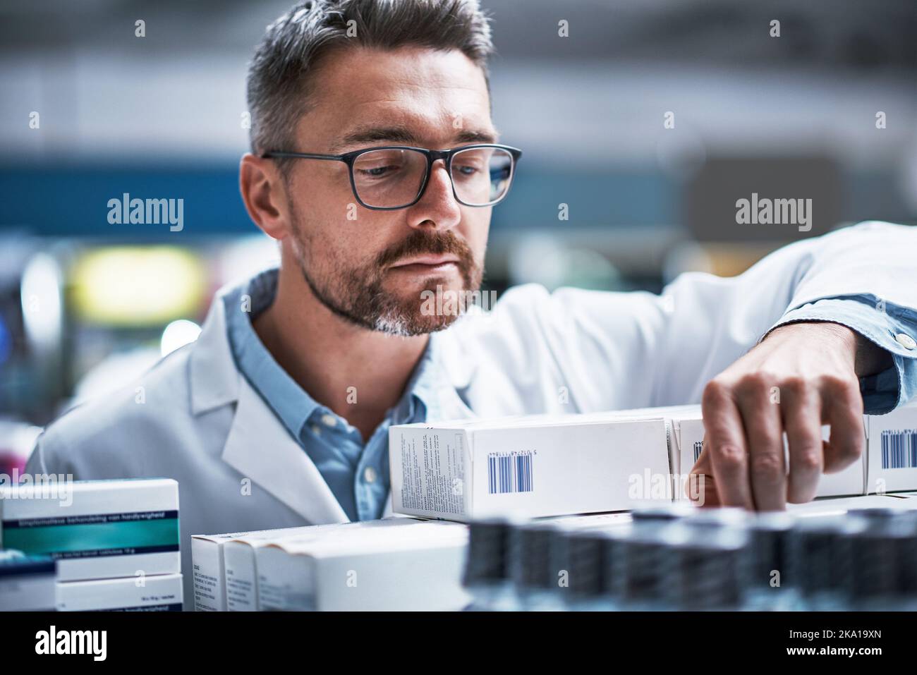 HES celui qui maintient les étagères bien approvisionnées. Un pharmacien mature vérifie les produits dans une pharmacie. Banque D'Images