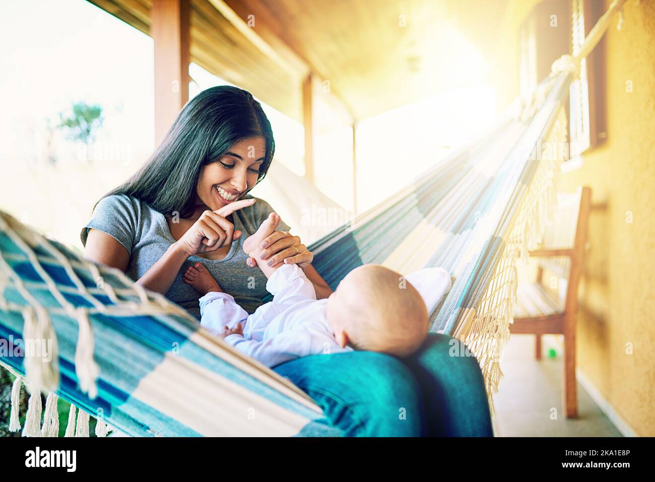 Regardez ces petits orteils. Une jeune mère gaie se détendant sur un hamac avec son fils bébé dehors à la maison pendant la journée. Banque D'Images