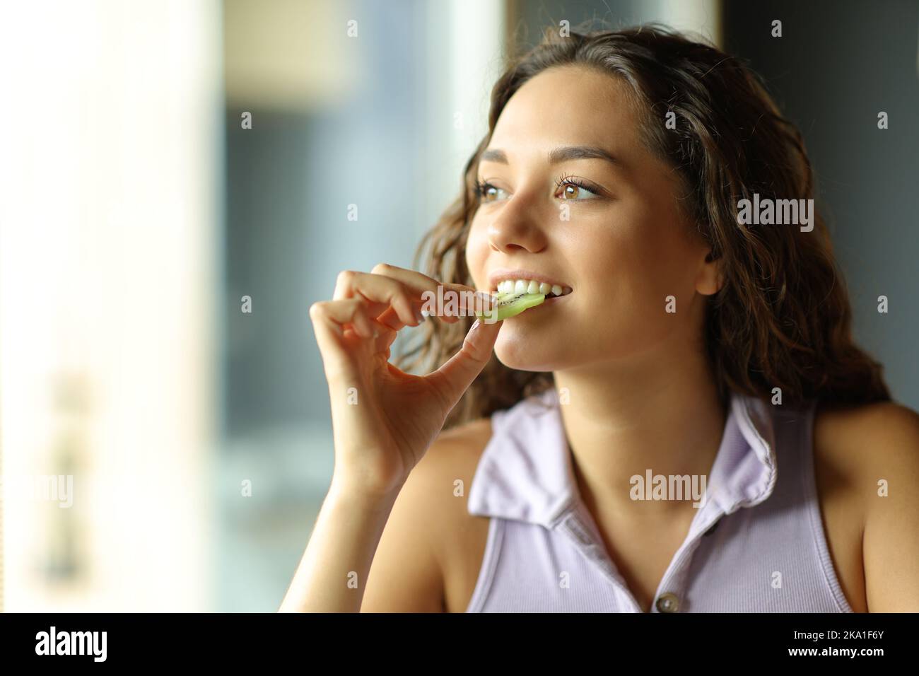 Bonne femme mangeant du kiwi à la maison en regardant par une fenêtre Banque D'Images