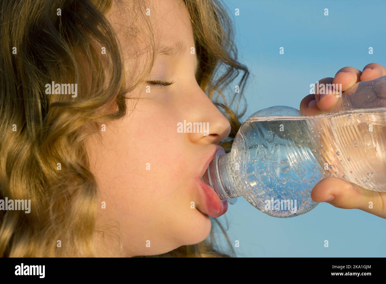 Une fille boit de l'eau minérale dans une bouteille pour animaux Banque D'Images