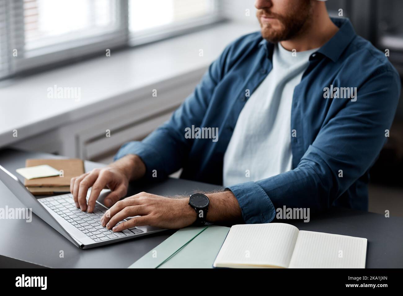 Gros plan d'un jeune homme qui tape sur le clavier d'un ordinateur portable tout en étant assis au bureau et en recherchant des informations en ligne ou en effectuant une mission Banque D'Images