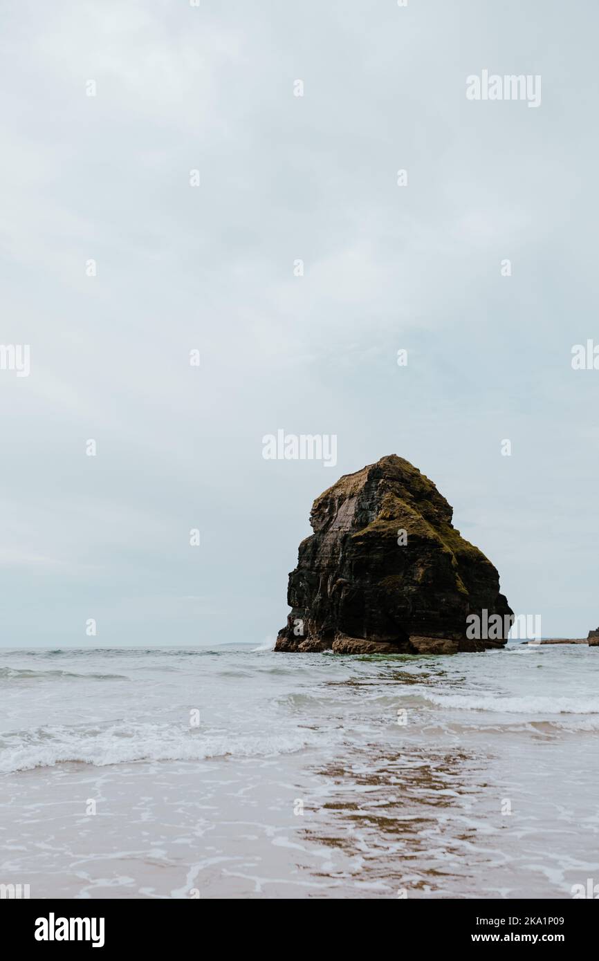 Une scène côtière avec des vagues qui se brisent doucement autour d'un rocher Banque D'Images