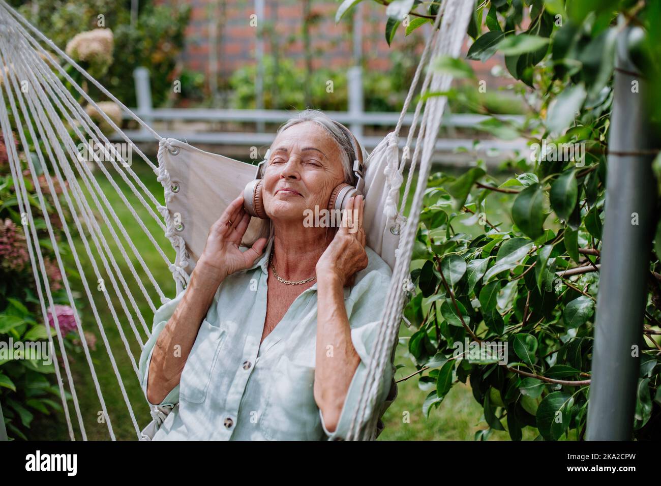 Femme sénior se détendant dans le jardin, écoutant de la musique à travers des écouteurs. Banque D'Images