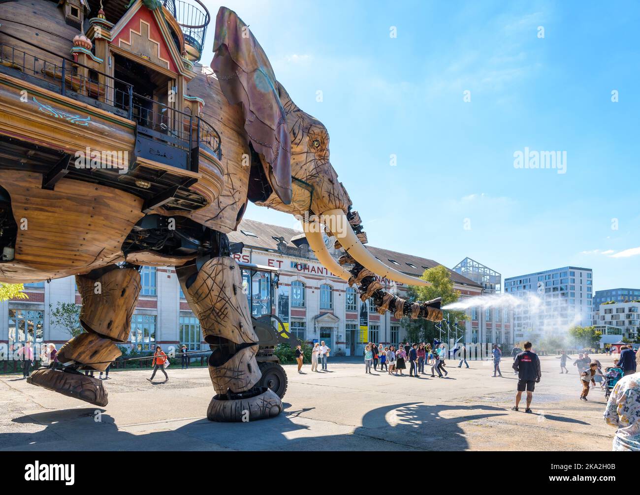La marionnette géante du grand éléphant, qui fait partie des machines de l'île de Nantes, pulvérise de l'eau avec son tronc sur les spectateurs le long du bâtiment des chantiers navals. Banque D'Images