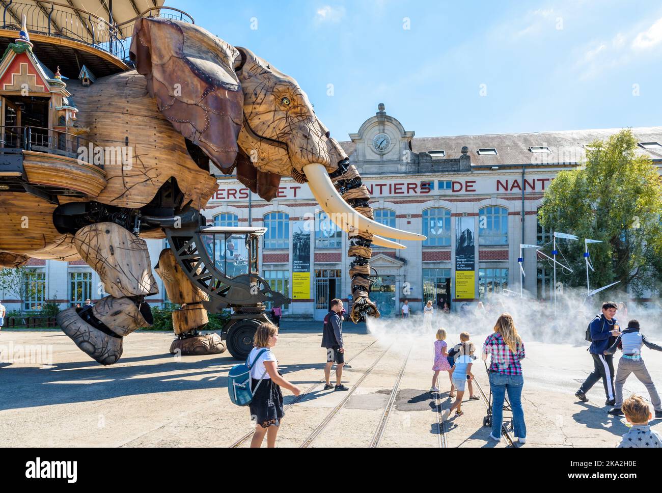 La marionnette géante du grand éléphant, qui fait partie des machines de l'île de Nantes, pulvérise de l'eau avec son tronc sur les spectateurs le long du bâtiment des chantiers navals. Banque D'Images