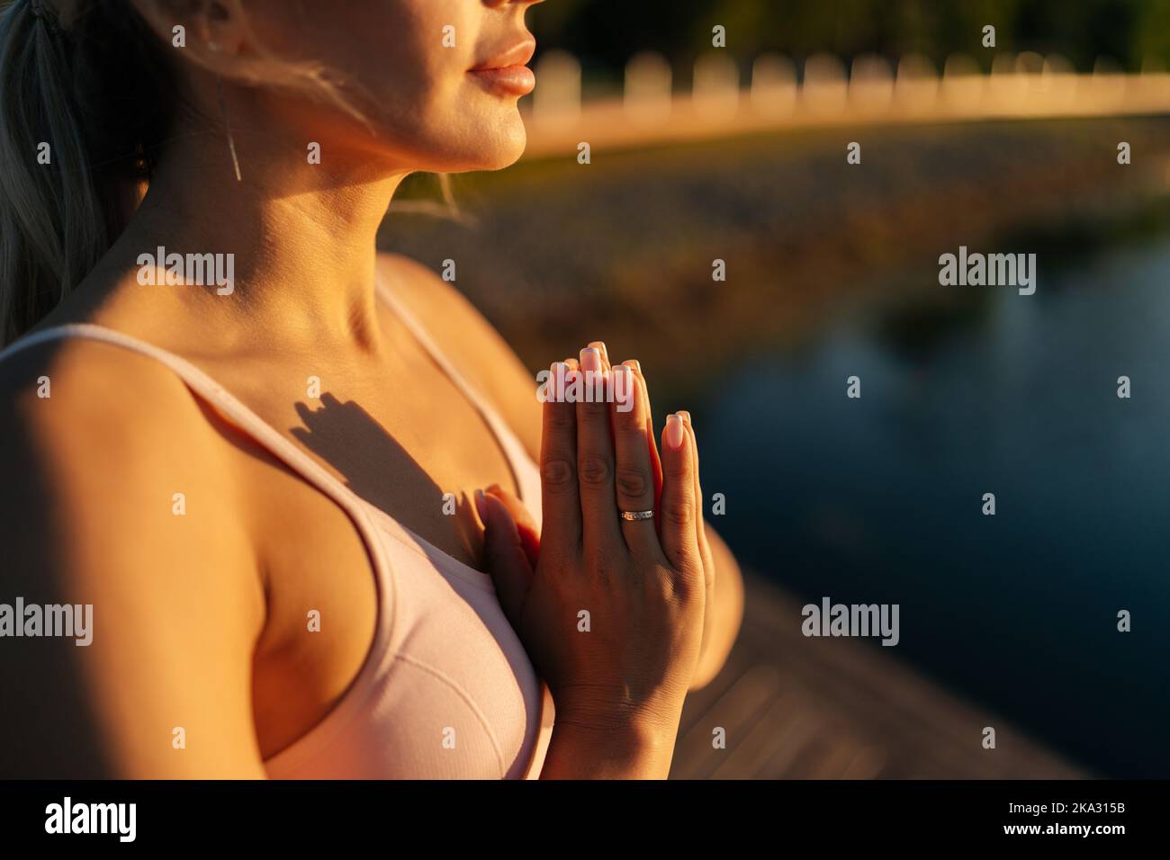 Gros plan court de la femme méditer tenant les mains dans un geste namaste debout près de l'eau dans la lumière douce du soleil le matin de l'été . Banque D'Images