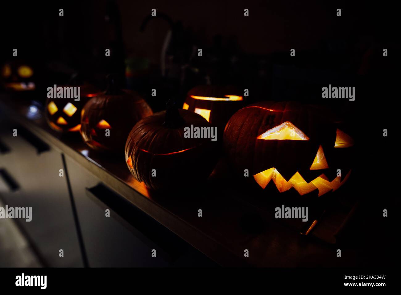Détails de faible profondeur de champ (mise au point sélective) avec diverses citrouilles d'Halloween sculptées (Jack-o-lanternes) dans l'obscurité avec bougies électriques à l'intérieur. Banque D'Images