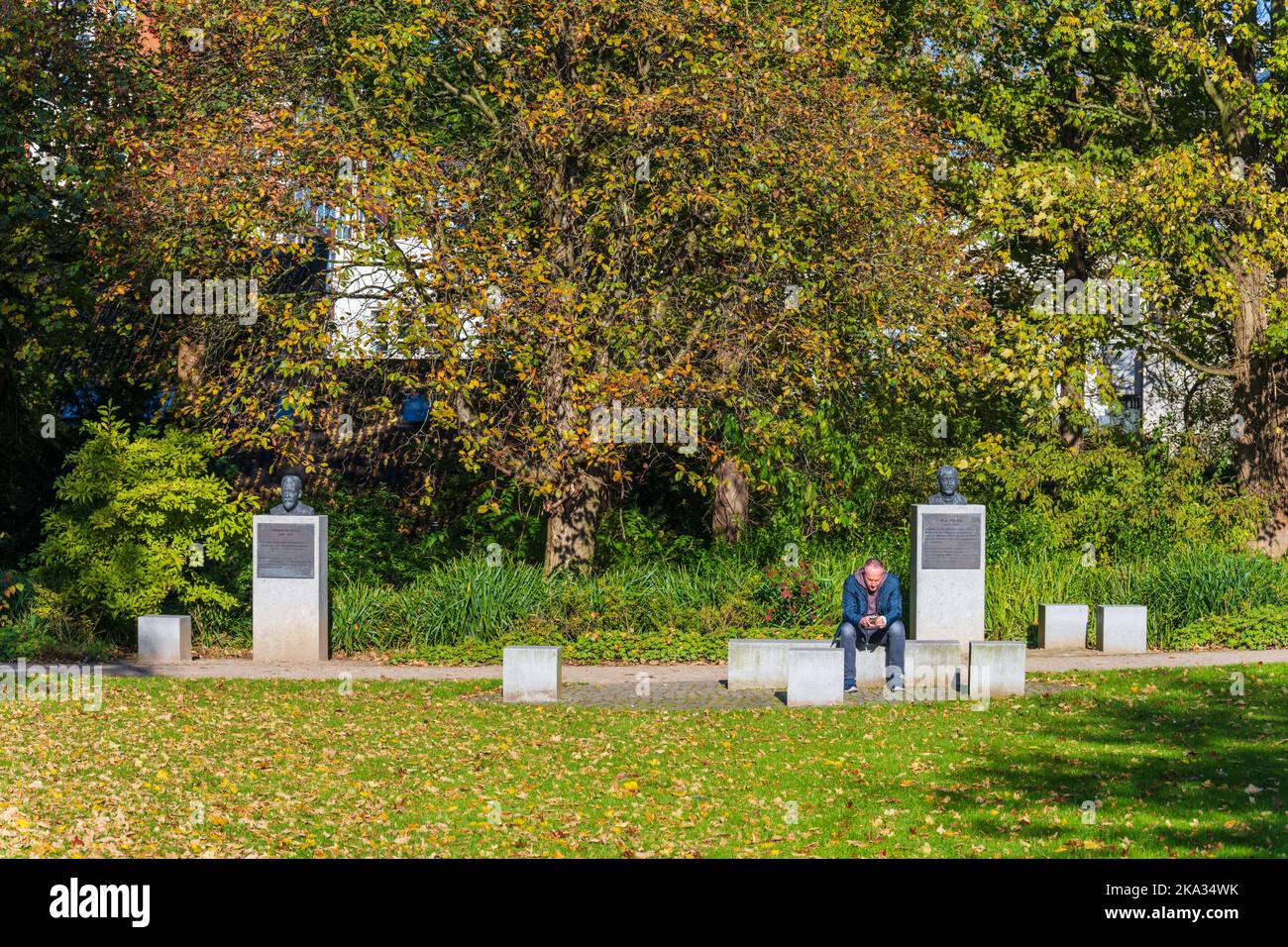 Herbstidylle Mann auf einer Stele sitzend im Ratsdienergarten in Kiel vor den Gedenksteinen der in Kiel an der Universität tätig gewesenen Nobelpreist Banque D'Images