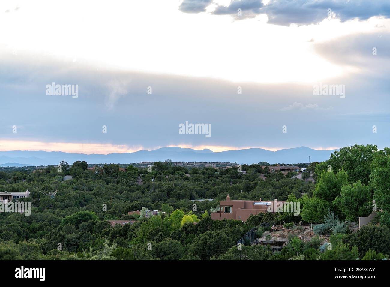 Coucher de soleil coloré à Santa Fe, Nouveau-Mexique avec feuillage vert élevé désert et paysage urbain bâtiments adobe maisons avec silhouette de montagnes en arrière-plan Banque D'Images
