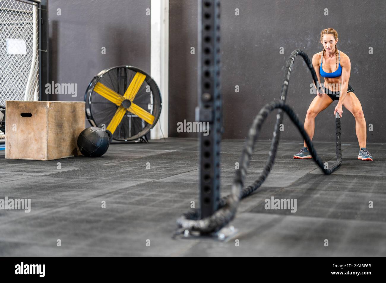 Athlète féminine pleine forme concentrée en forme d'activewear faisant de l'exercice avec des cordes de combat pendant l'entraînement physique intense en salle de gym Banque D'Images