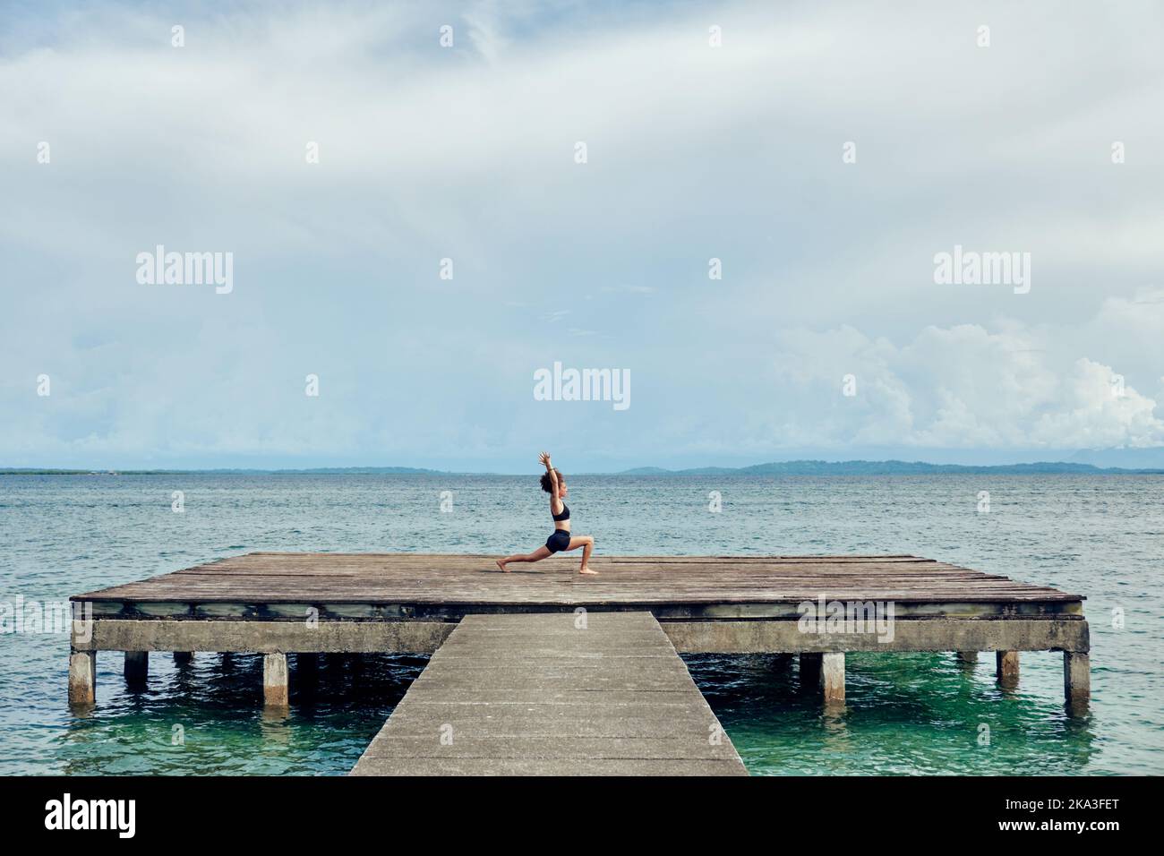 Femme éloignée en casque d'activité noir exécutant Ashta Chandrasana avec les bras vers le haut contre la mer paisible Banque D'Images