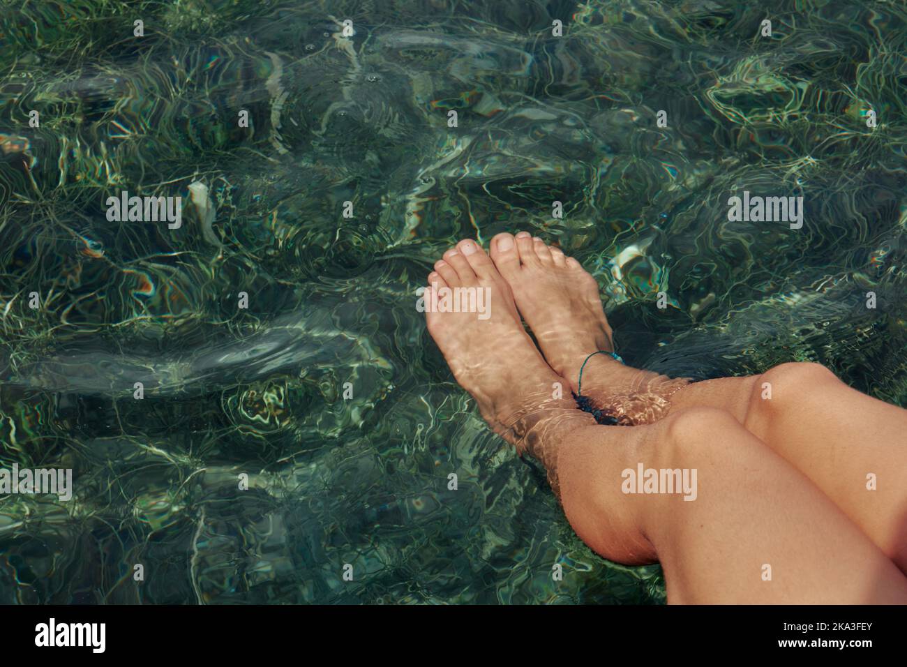 Par le dessus, les jambes de femme ethnique non reconnaissables sont écourtées sur une jetée en bois avec des jambes dans de l'eau bleue claire Banque D'Images