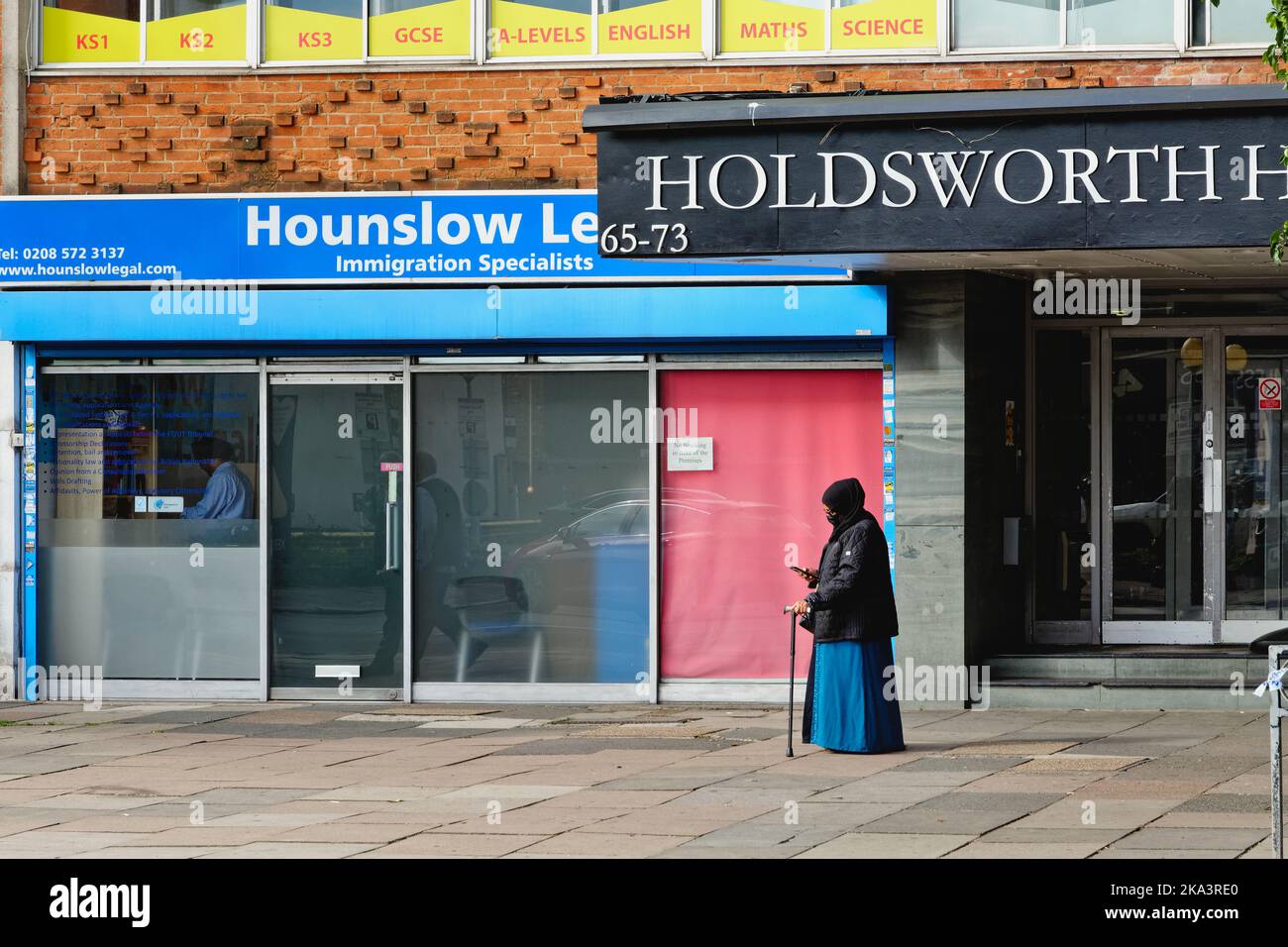 Une femme musulmane âgée avec un bâton de marche debout devant un bureau traitant des affaires d'immigration à Hounslow West London Angleterre Banque D'Images