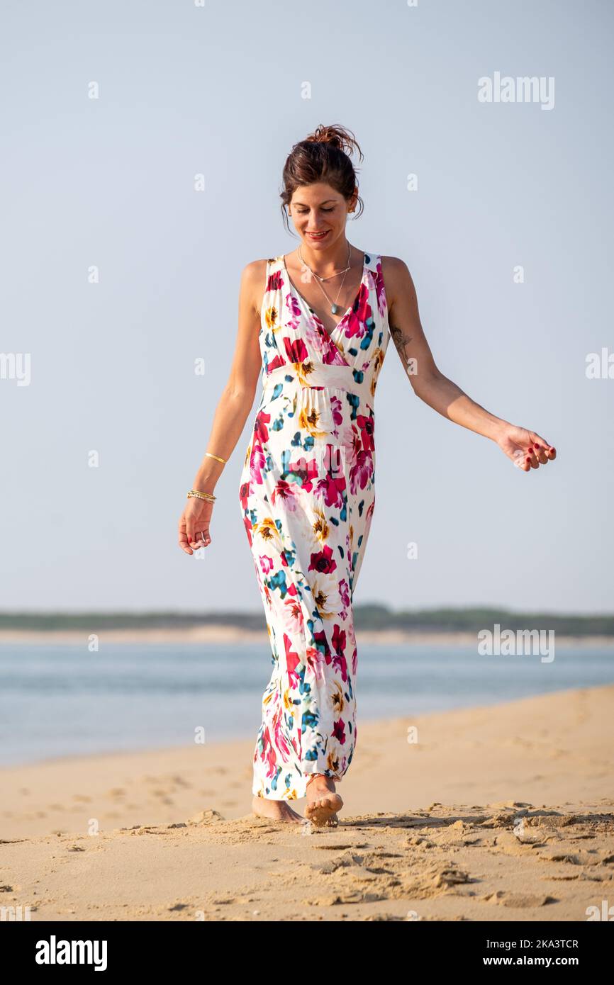 Belle femme souriante dans une robe maxi marchant sur la plage en été, France Banque D'Images