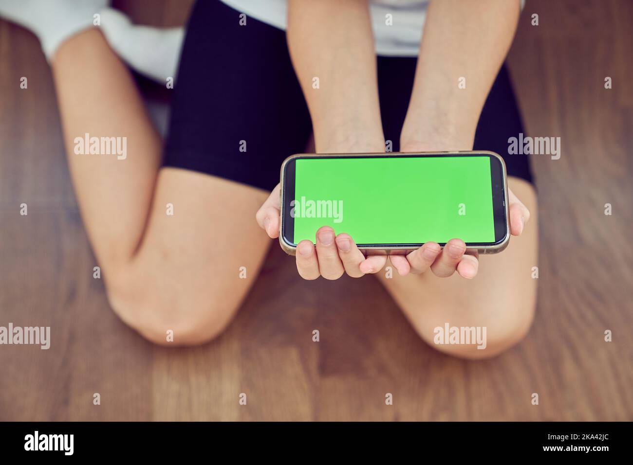 Gros plan des mains d'Une fille qui s'assoit sur le sol et utilise un téléphone avec un écran vert. Une maquette de smartphone avec un espace de copie pour votre produit. Photo de haute qualité Banque D'Images Gros plan des mains d'Une fille qui s'assoit sur le sol et utilise un téléphone avec un écran vert. Une maquette de smartphone avec un espace de copie pour votre produit. Photo de haute qualité Banque D'Images