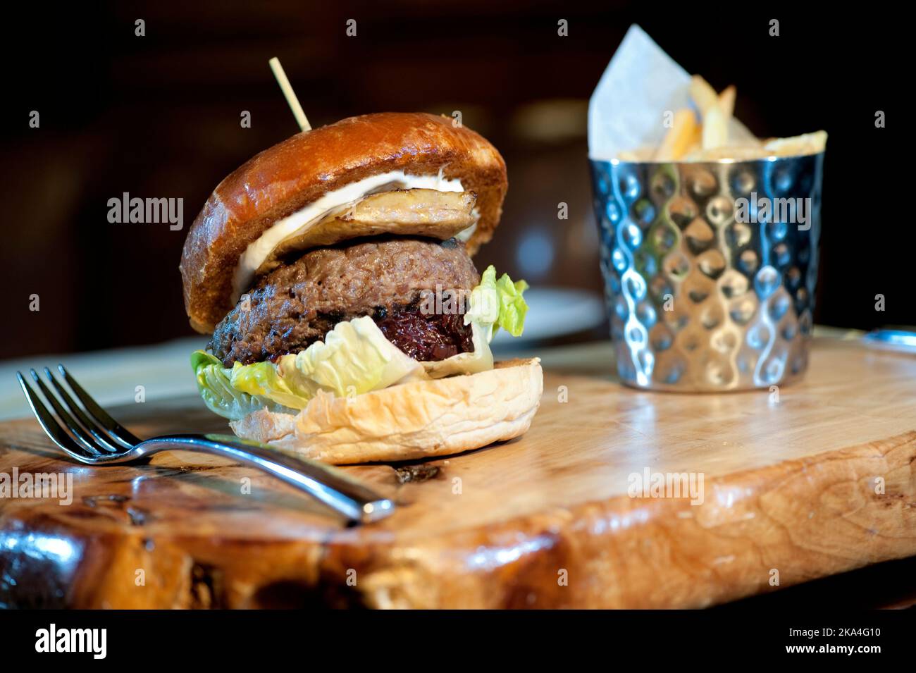 Grand hamburger à l'oignon rouge caramélisé et frit à la française servi sur une planche à découper en bois Banque D'Images