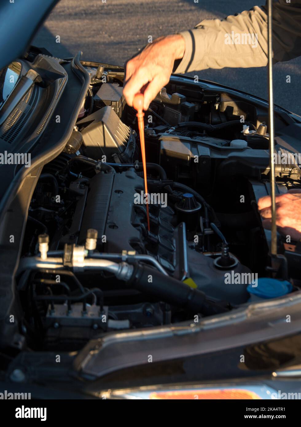 Voiture avec le capot ouvert et une personne, un homme plus âgé, vérifiant ou travaillant sur la voiture. Banque D'Images