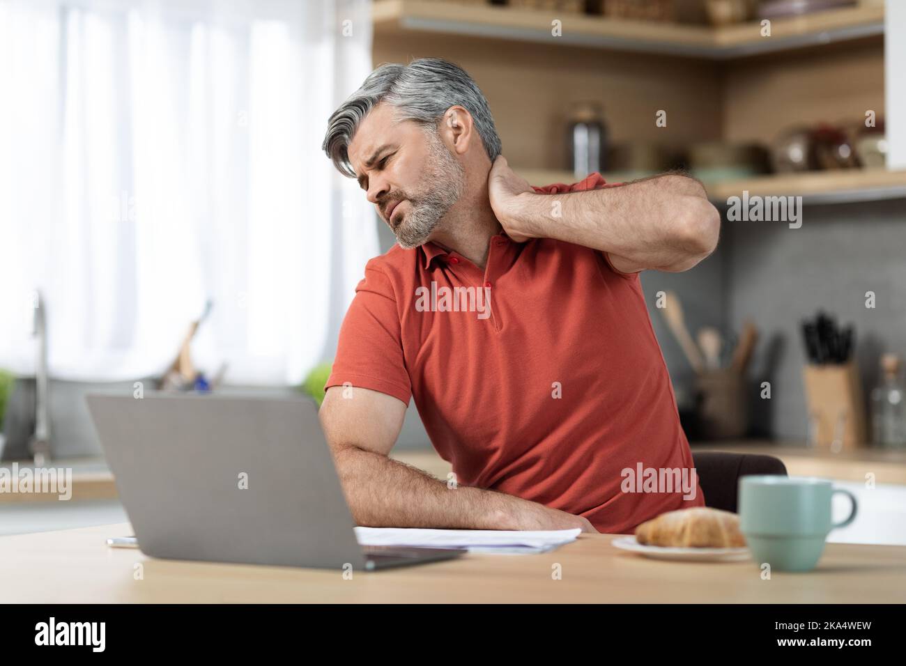 Homme fatigué assis devant l'ordinateur portable, touchant le cou Banque D'Images