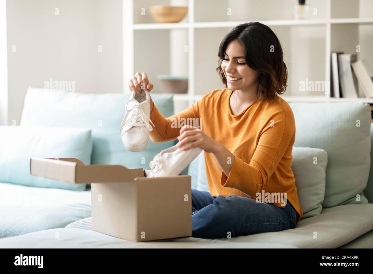 Portrait de la jeune femme arabe heureuse unboxing colis avec des chaussures à la maison Banque D'Images