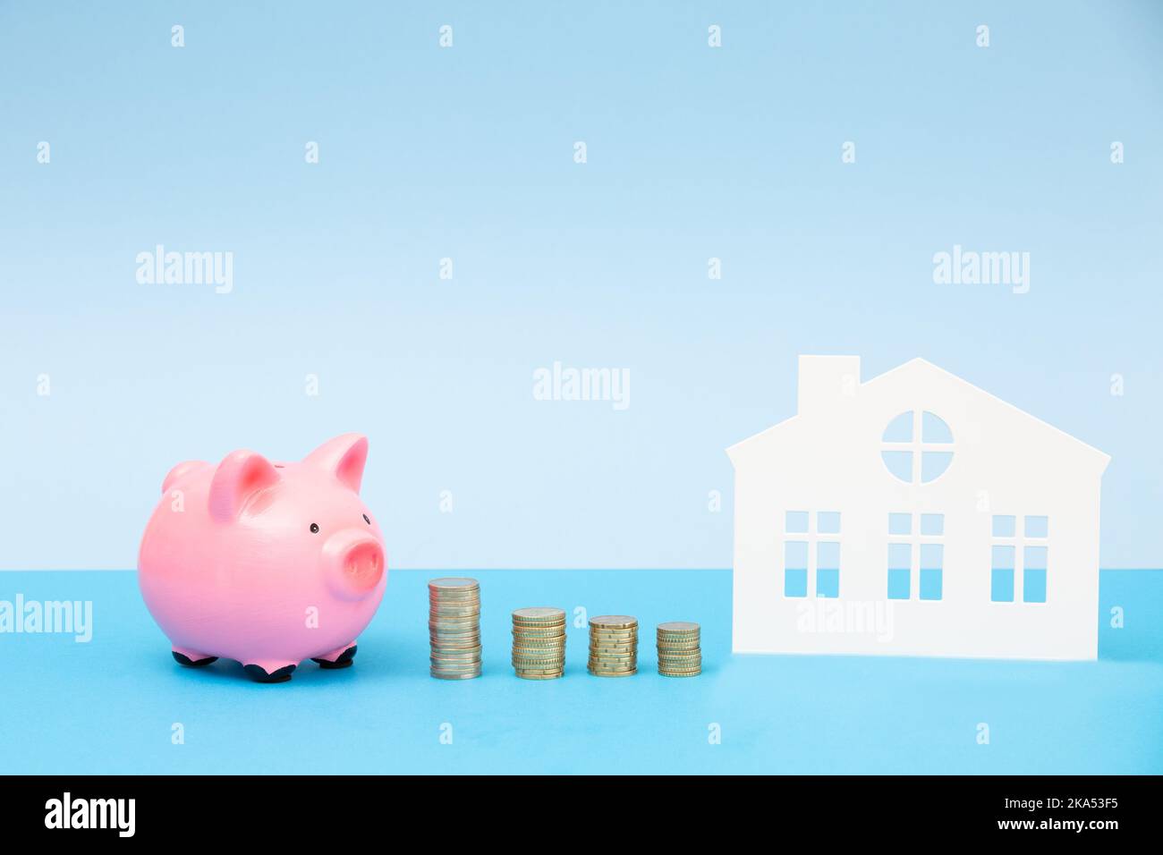 Banc de piggy rose avec des piles de pièces de monnaie à côté de la maison. Le concept de l'investissement dans l'immobilier, dans l'avenir, l'épargne, la planification financière. Banque D'Images