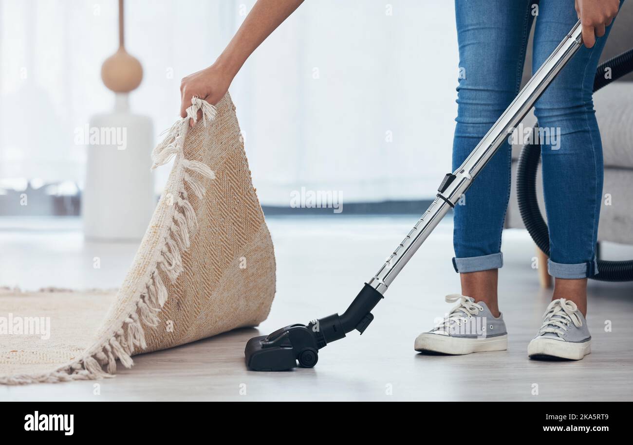 Aspirateur, sol et femme nettoyant sous un tapis dans le salon d'une maison. Le ménage, le service et le nettoyage passent l'aspirateur dans le salon avec un tapis ou Banque D'Images