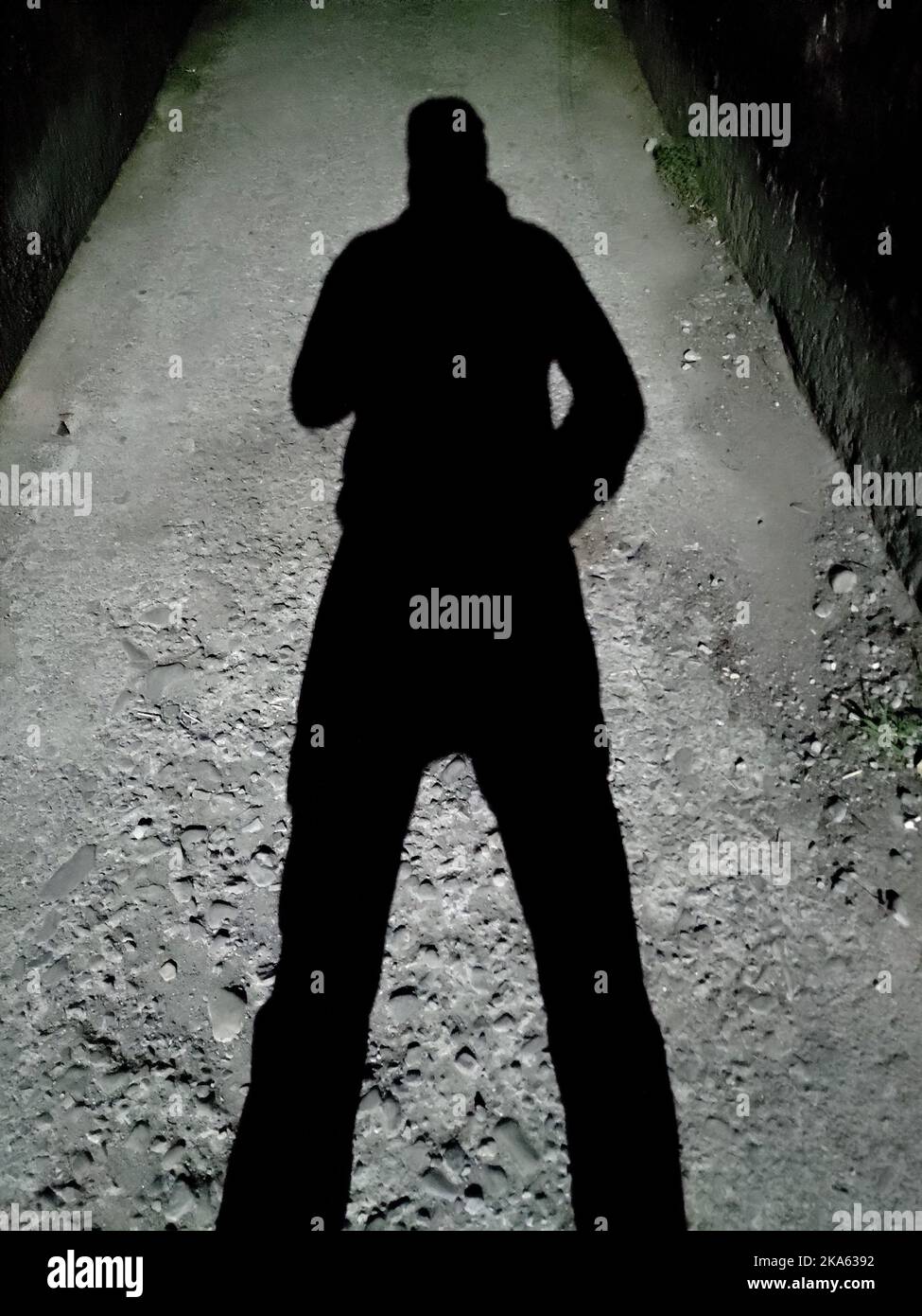 Homme jetant une ombre contre un lampadaire dans une ruelle sombre la nuit. Inde. Banque D'Images