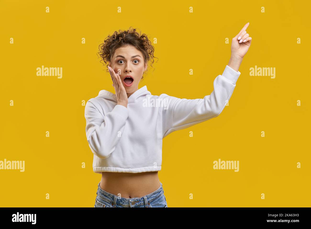 Vue avant de jolie fille avec des cheveux bouclés debout surpris, choqué. Belle jeune femme touchant le visage avec la bouche ouverte, pointant par le doigt. Isolé sur un bacille jaune. Banque D'Images Vue avant de jolie fille avec des cheveux bouclés debout surpris, choqué. Belle jeune femme touchant le visage avec la bouche ouverte, pointant par le doigt. Isolé sur un bacille jaune. Banque D'Images