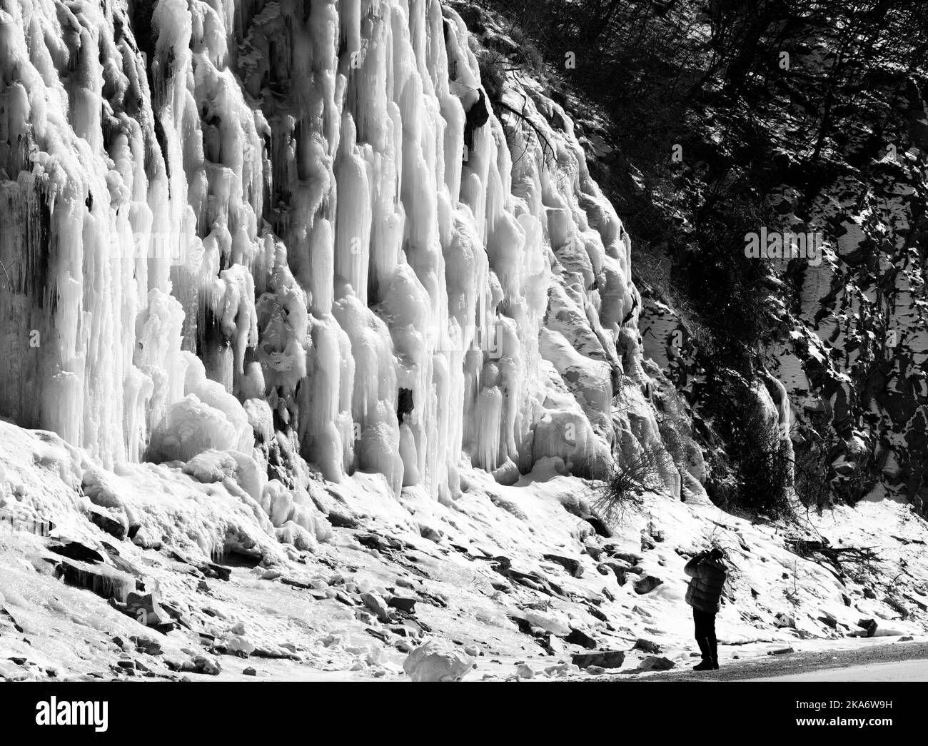 L'homme fait une photo de la cascade de montagne glacée à un beau jour de soleil. Hiver en Géorgie. Image en noir et blanc. Banque D'Images