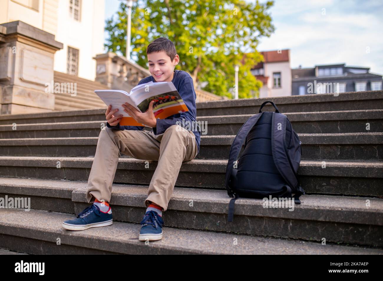 Un adolescent mignon lisant un livre assis sur les escaliers Banque D'Images