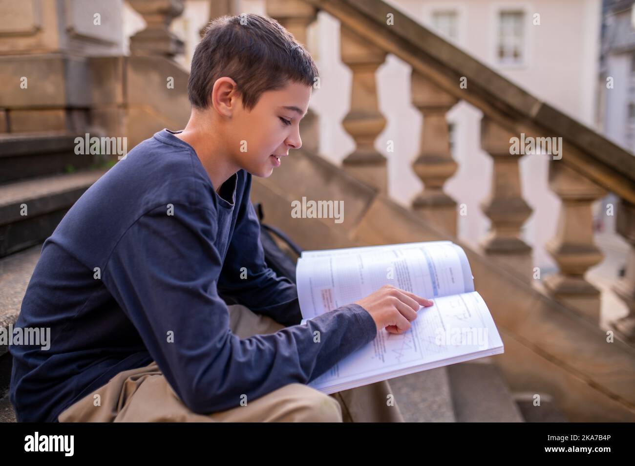 Adolescent en perce un livre assis sur les marches en béton à l'extérieur Banque D'Images