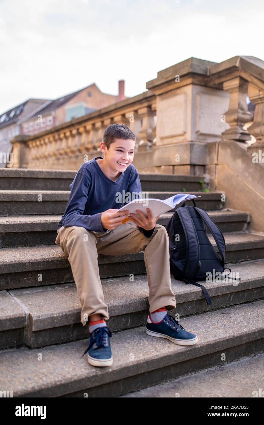 Joyeux adolescent avec un livre assis sur les escaliers Banque D'Images