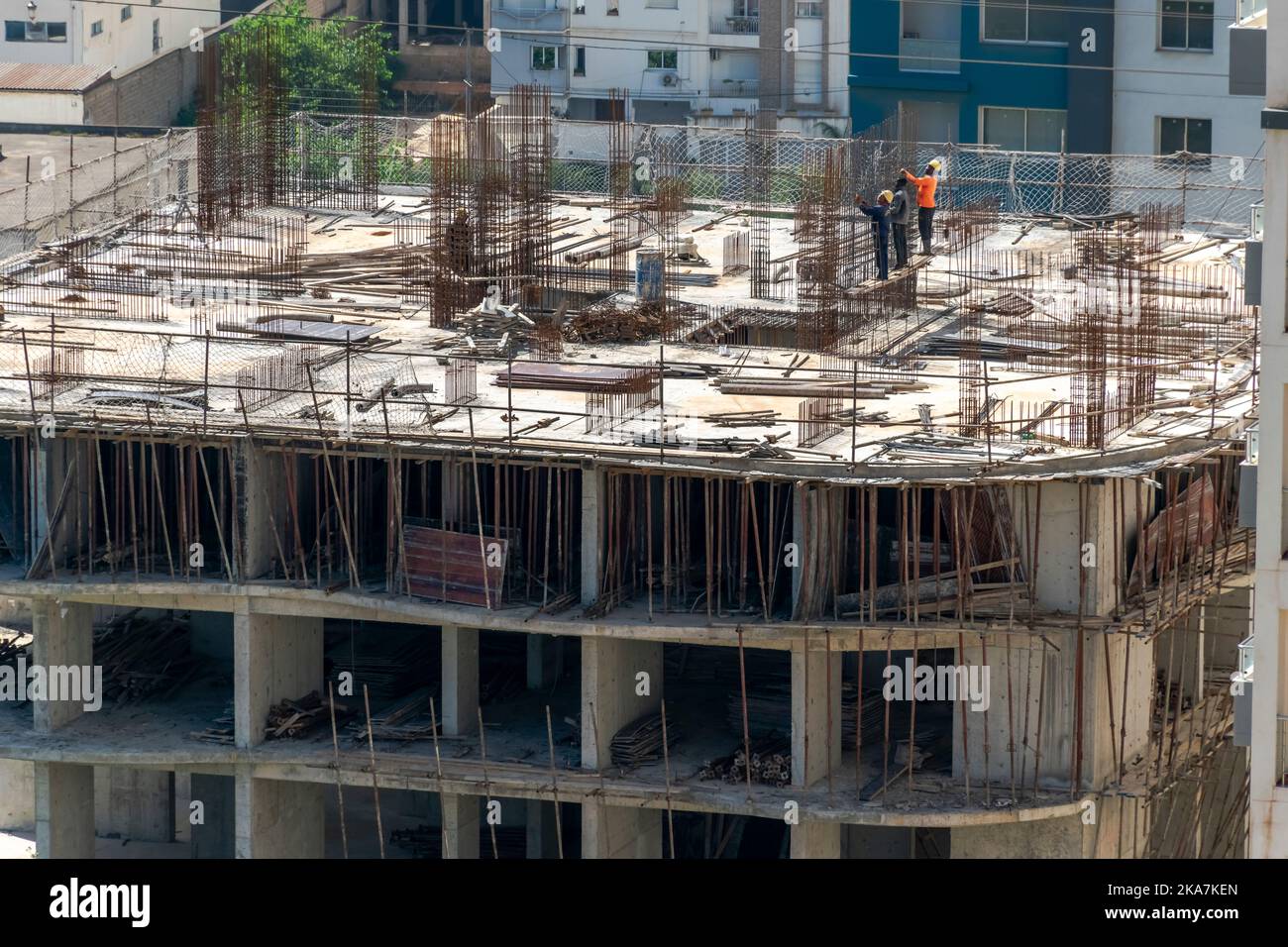 des ouvriers chinois et africains noirs sur le toit d'un chantier de construction occupé avec du ferrobéton par temps ensoleillé. Banque D'Images